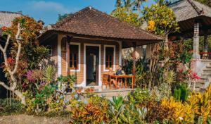 a woman sitting at a table in front of a small house at Pondok Lembah Dukuh Homestay in Tirtagangga