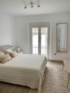 a white bedroom with a large bed and a mirror at La Casa del Puente in Lecrin