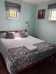 a bedroom with a bed with a comforter and two windows at Cabañas Campestres Las Rosas in Punta Arenas