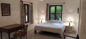 a bedroom with a bed and a table and two windows at Isai Ambalam guest house in Puducherry