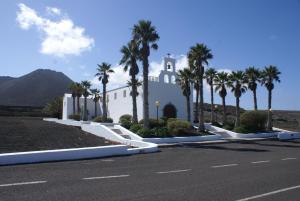 a church with palm trees in front of a road at VolKKanrentals Casa Machín in Famara