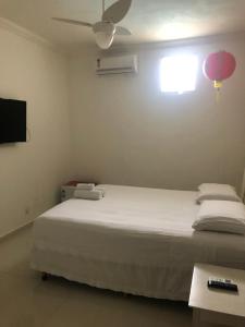 um quarto com uma cama branca e uma ventoinha de tecto em Suites Praia de Pernambuco no Guarujá
