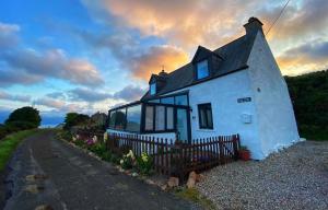 a small white house with a fence next to a road at Piper's Cave bed and breakfast in Helmsdale