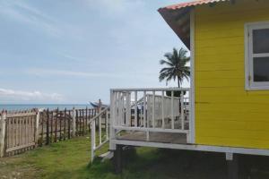 una casa amarilla con un porche junto a una valla en La Casa Amarilla (Sobre las playas del mar Caribe), en San Bernardo del Viento
