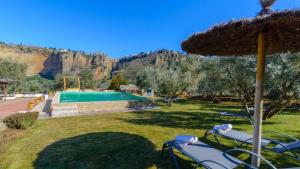 a lawn with chairs and an umbrella and a pool at Casa El Puente Ronda by Ruralidays in Ronda