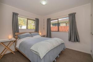 a bedroom with a large bed and two windows at Hosts on the Coast Cosy on Cath in Whitianga