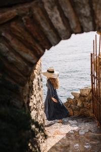 a woman in a hat sitting on a wall near the water at BYPILLOW Cap Sa Sal in Begur