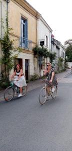 two women in dresses riding bikes down a street at L'arbrissel in Fontevraud-l'Abbaye