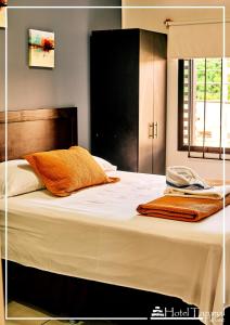 Una cama con sábanas blancas y almohadas naranjas. en Hotel Tazumal House en San Salvador