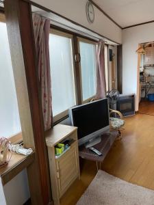 ein Wohnzimmer mit einem TV und einem Schreibtisch mit einem Monitor in der Unterkunft City Otaru in Otaru
