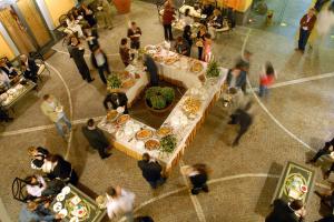 una multitud de personas de pie alrededor de una mesa con comida en City Hotel, en Casoria
