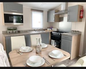 a kitchen with a wooden table with plates and wine glasses at Exotic 3-Bed Caravan at Newquay Holiday Park in Newquay