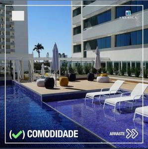 uma piscina com cadeiras e guarda-sóis ao lado de um edifício em Flat Apart Hotel América Campos dos Goytacazes em Campos dos Goytacazes