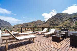 a deck with chairs and tables with mountains in the background at Apartamentos Los Telares in Hermigua