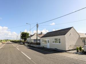 an empty street with a white house on the side of the road at Bwthyn Tyn y Coed in Bryngwran