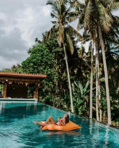 una mujer acostada sobre una almohada naranja en una piscina en The Artini Dijiwa Ubud en Ubud