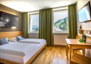 a hotel room with a bed and a desk and windows at JUFA Hotel Schladming in Schladming