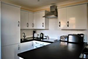 uma cozinha com armários brancos e um balcão preto em The Old Schoolhouse Hotel em Larkhall