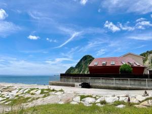 a red building with a red roof next to the ocean at Seaside SHELL HOUSE -南房総 海辺のSHELL HOUSE- in Minamiboso