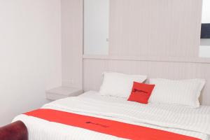 a white bed with a red pillow on it at RedDoorz near Exit Tol Kotabaru ITERA Lampung in Kedaton