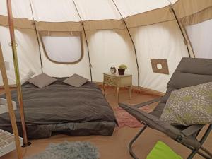 Natuur-like Glamping in Bosland في Neerpelt: غرفة نوم بسرير وكرسي في خيمة