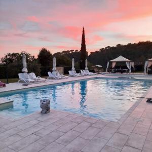 a swimming pool with white chairs and a sunset at Il Casolare Val Di Mare in Riparbella