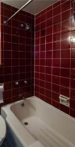 W wyłożonej czerwonymi kafelkami łazience znajduje się biała wanna. w obiekcie Curtis Gordon Motor Hotel w mieście Winnipeg