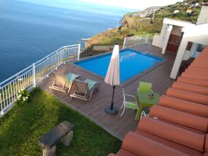 a swimming pool with chairs and an umbrella next to the ocean at CASA SOL E VISTA 2 in Arco da Calheta