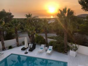 a resort with a pool and palm trees and the sunset at Can Love in Cala Comte
