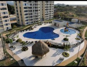 a large swimming pool with a straw umbrella and buildings at Lindo apartamento cerca a Girardot in Ricaurte