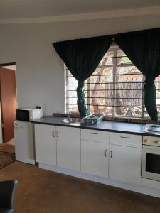 cocina con armarios blancos y ventana grande en Dombeya Ridge Guest Suite, en Rustenburg