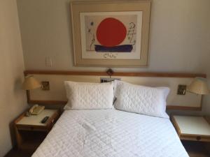 um quarto com uma cama branca, 2 mesas de cabeceira e um telefone em Flat Golden Plaza - Lourdes em Belo Horizonte