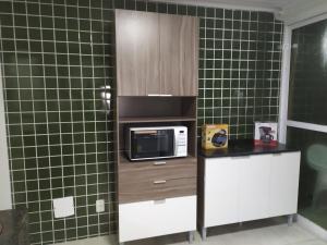 a kitchen with a microwave and green tiled walls at Cobertura Fort do Pontal in Arraial do Cabo
