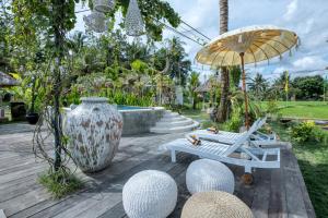 eine Terrasse mit einer Bank, einem Regenschirm und einer Vase in der Unterkunft The Rice Joglo Eco-Stay in Ubud