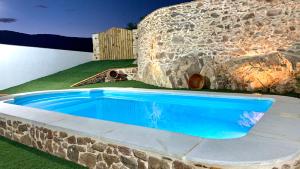 a blue swimming pool in front of a stone wall at Casa Rural Sierra Tórtola 2 in Hinojales