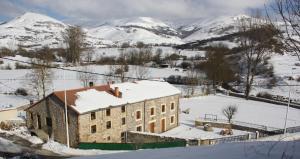 un bâtiment recouvert de neige avec des montagnes en arrière-plan dans l'établissement Palomba Rural, à Espinilla