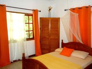 a bedroom with a bed with orange curtains and a window at Chalets Anse Possession in Baie Sainte Anne