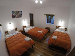 a room with three beds with orange sheets at Tucan Hostel in Cusco