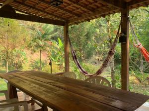 une table en bois avec des chaises et un hamac sur une terrasse couverte dans l'établissement Chalé Hakuna Matata, à Lumiar