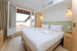 a bedroom with a large white bed and a balcony at Hôtel Les Grenettes in Sainte-Marie-de-Ré