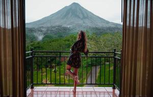 Una mujer parada en un balcón con vistas a una montaña en Hotel Arenal Kioro Suites & Spa, en Fortuna