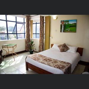 1 dormitorio con cama, mesa y ventanas en Hopewell Guest House, en Nyeri