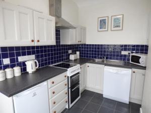 a kitchen with white cabinets and blue tiles on the wall at Hafod Cottage in Cemaes Bay +9 photos