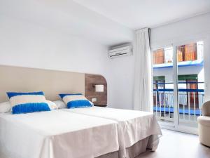 a white bedroom with a large bed with blue pillows at Hotel Flats Friends Mar Blau in Benidorm