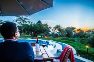 Eine Frau, die mit einem Glas Wein am Tisch sitzt. in der Unterkunft Kigambira Safari Lodge in Bakijurura