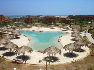 a large pool with straw umbrellas in a resort at Marina Wadi Degla A Ground Chalet Near to the Beach in Ain Sokhna in Ain Sokhna