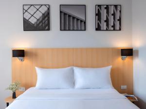 a bedroom with a white bed and three pictures on the wall at Ibis Bangkok Sukhumvit 4 in Bangkok