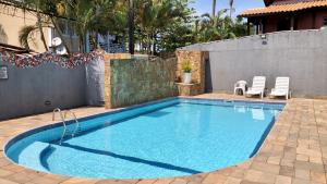 a swimming pool with two white chairs next to a house at Pousada Raio de Sol Maresias in Maresias