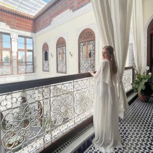 une femme en robe blanche debout sur un balcon dans l'établissement Riad Alassala Fes, à Fès