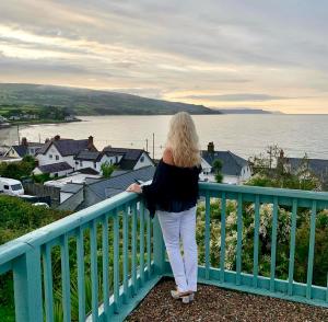 拉恩Ballygally Seaview Cottage的站在一个水景阳台上的女人